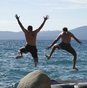 Two young men jump in the air with Lake Tahoe in the background.
