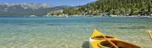A yellow kayak rests on the shore of Lake Tahoe facing the water.