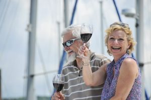 A retired couple strolls by the boats with wine in hand.