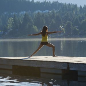 A woman holds a warrior pose on a boat dock with the lake in the background.