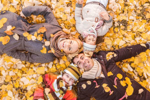 family of four laying on yellow fall leaves smiling for photo
