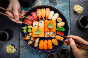 Set of sushi and maki with soy sauce with human hands over blue background. Top view with copy space